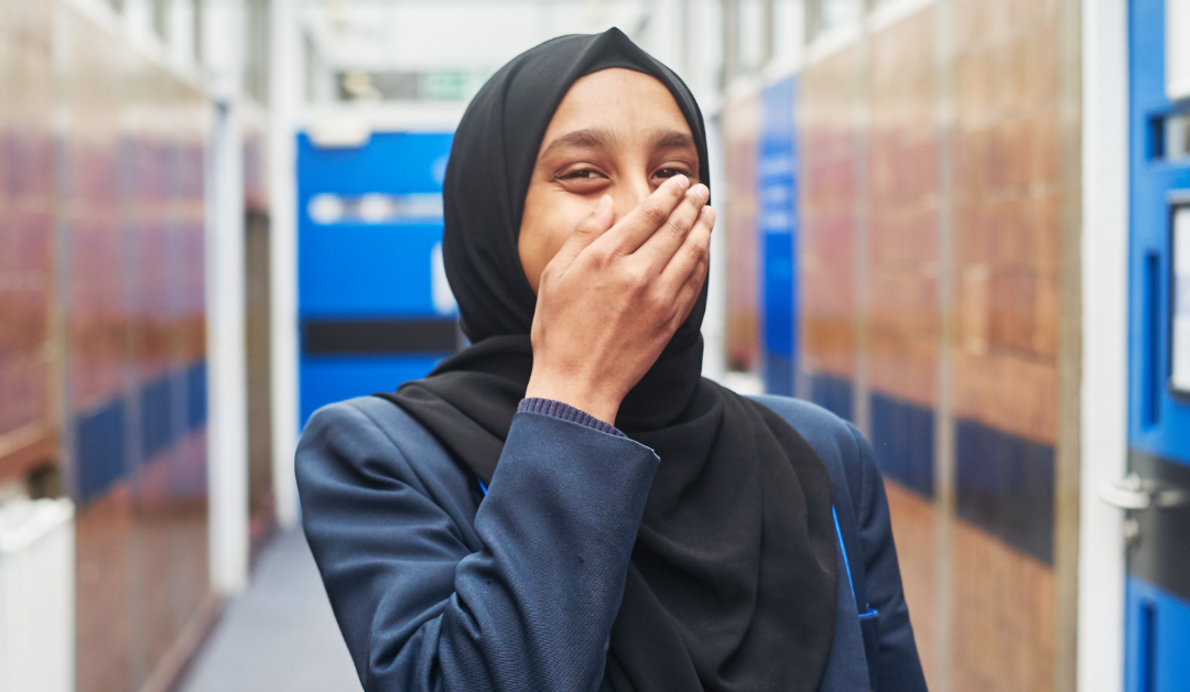 Image of a young woman covering her mouth looking happy